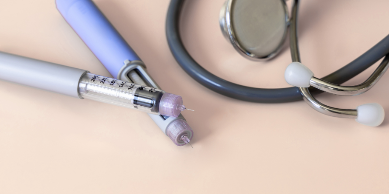 Two medication injection pens with needles attached, with a stethoscope next to them.
