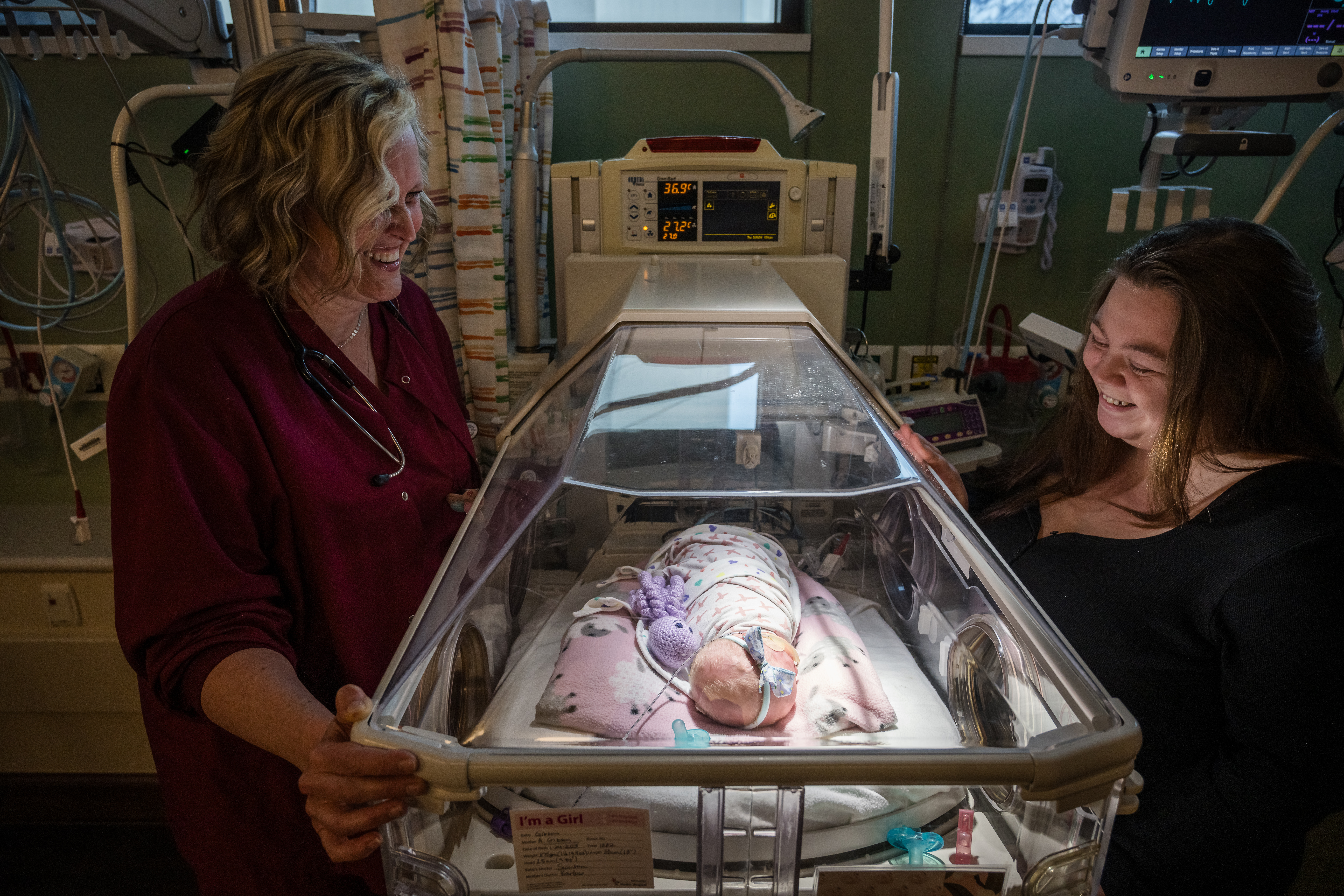 NICU nurse and Alyssa standing near isolette with baby Elenor in it