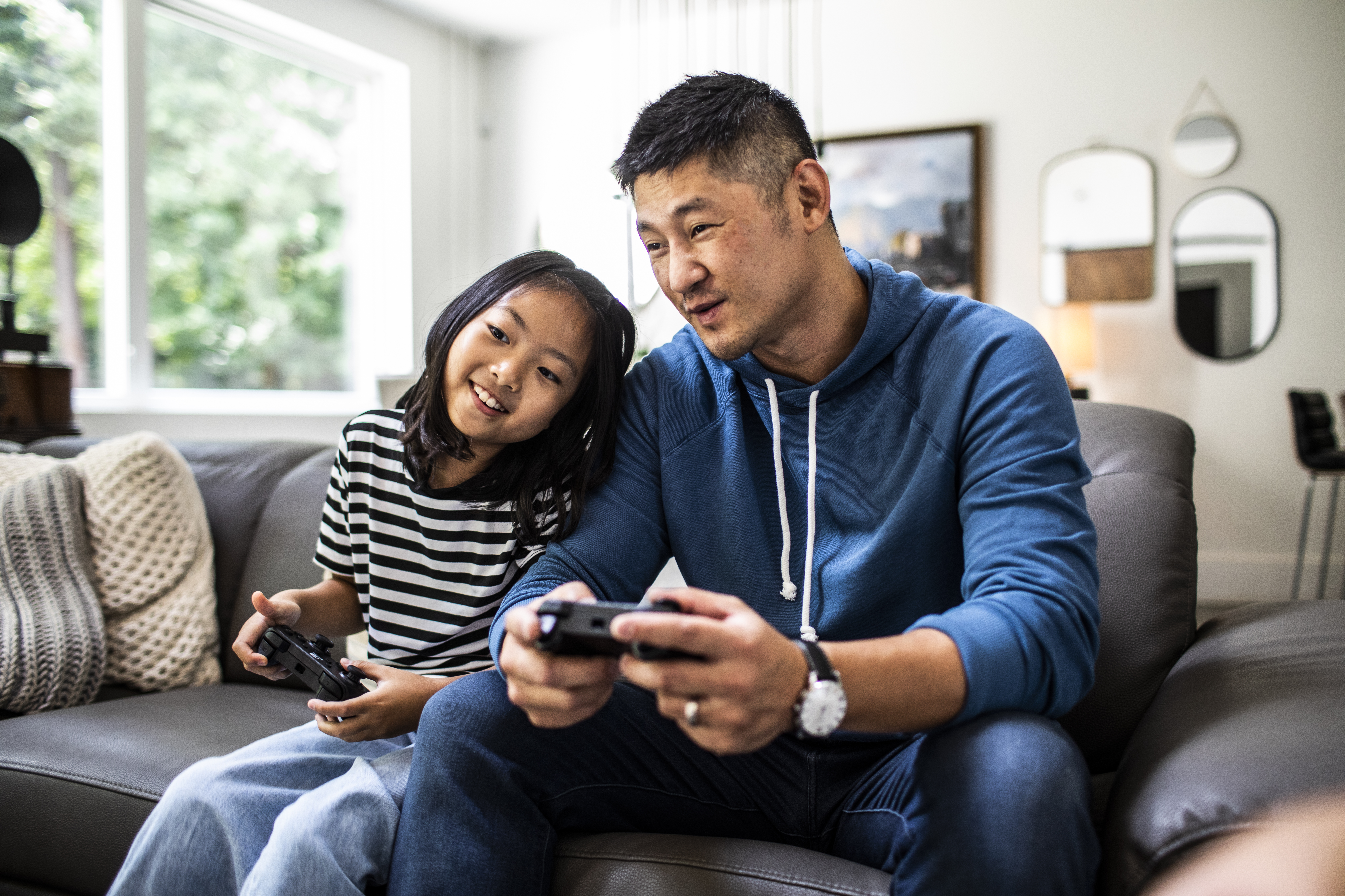 Father and daughter sitting on a couch playing video games.