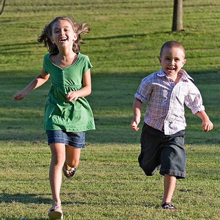 Two children smile and laugh while running in the grass.