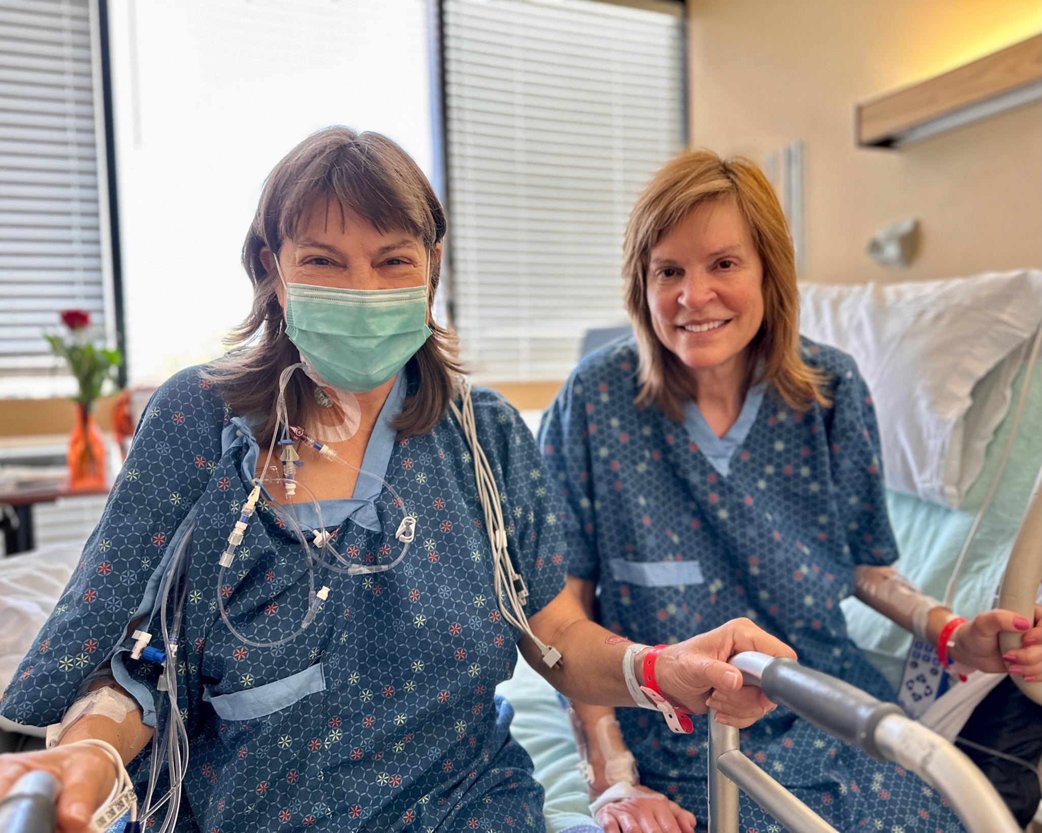 Carol Kenny and Janet Hill sitting on hospital bed, seeing each other for the first time after surgery