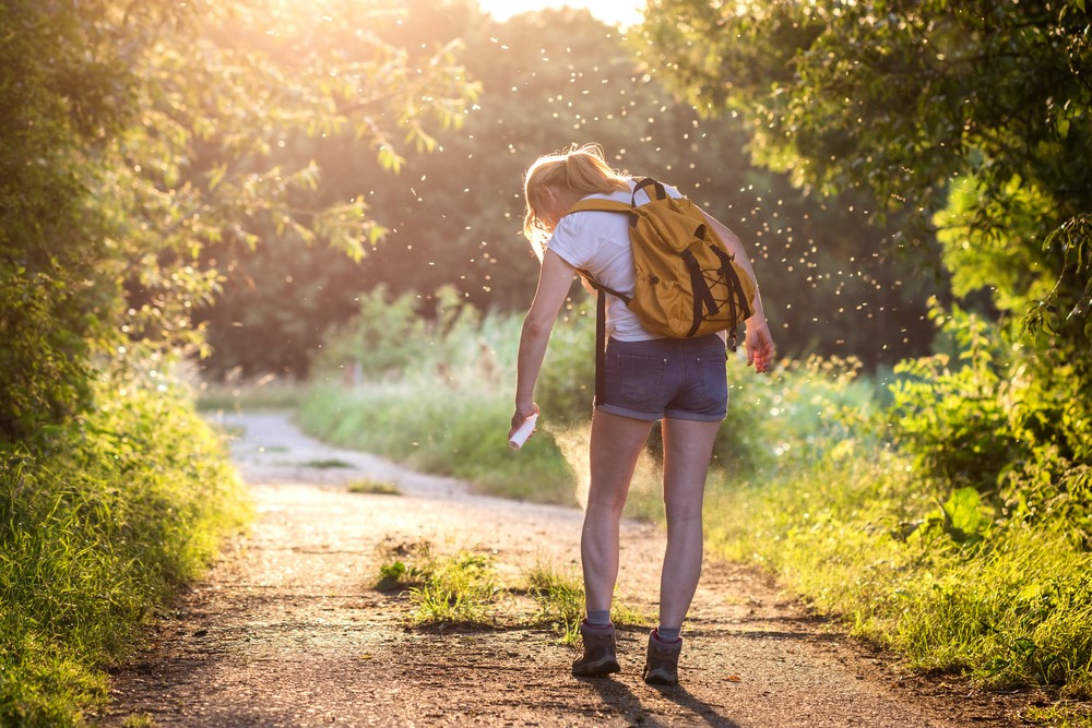 Woman walking on path spraying insect repellant on leg