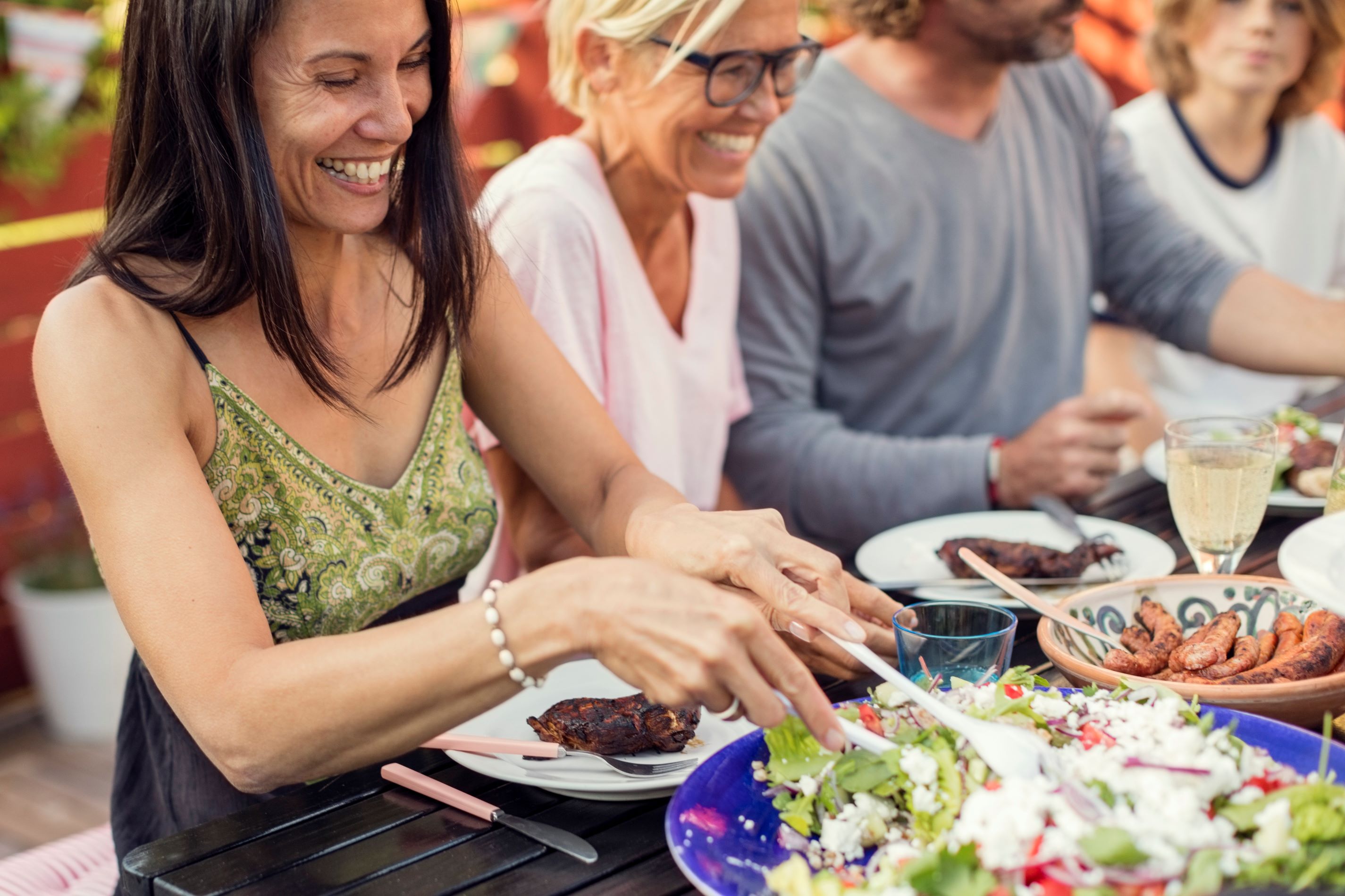 A variety of people eating at an outdoor table sharing a healthy meal including salad