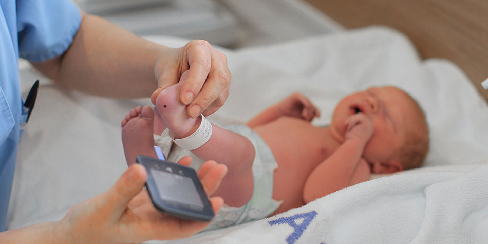 A nurse performs a blood test on a newborn baby, by testing the bottom of its foot.