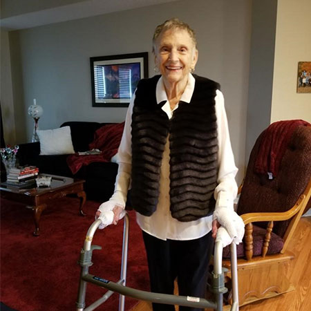 Pat smiles while standing with her walker in her living room.