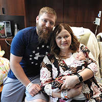 Morgan and Josh Howell smile while holding their newborn daughter in the hospital.