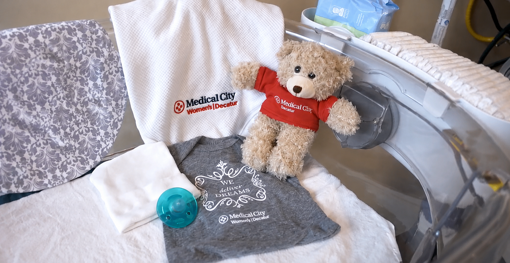 Nursery crib with medical city teddy bear, blanket, and other crib accessories.