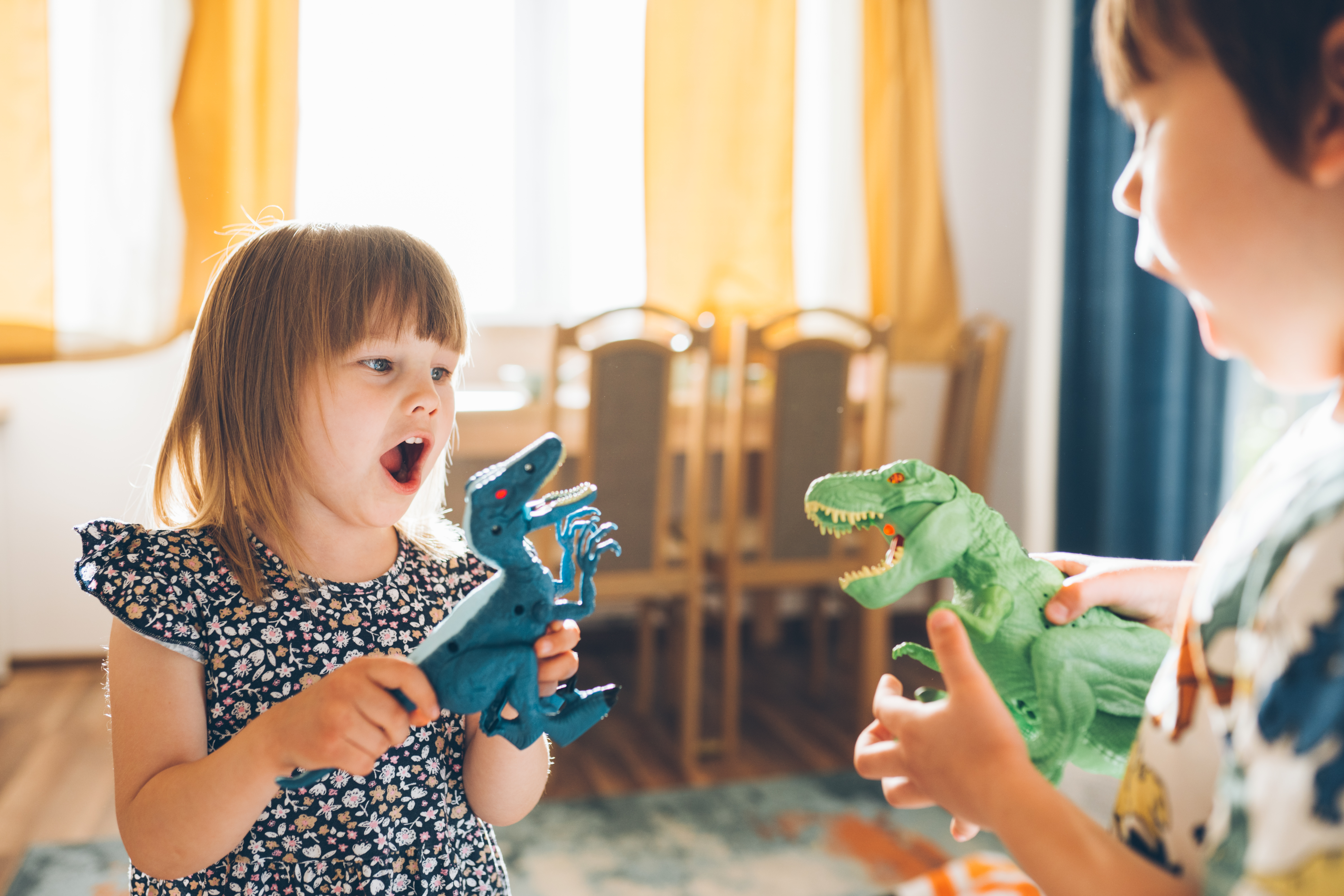 Two children play with dinosaur toys in the living room.