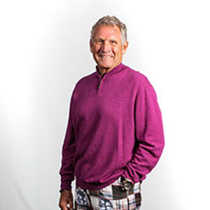 Larry smiles while wearing a plum colored polo with blue and white plaid pants.