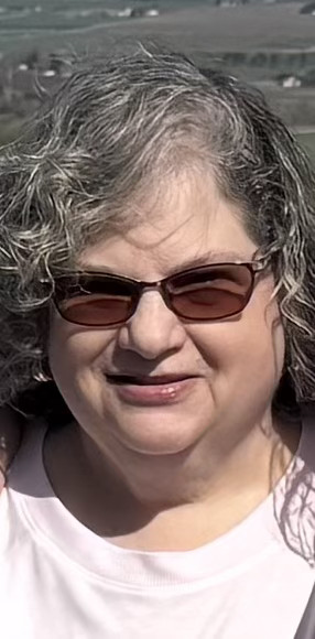 Photo showing of a woman wearing sunglasses and smiling for a picture.