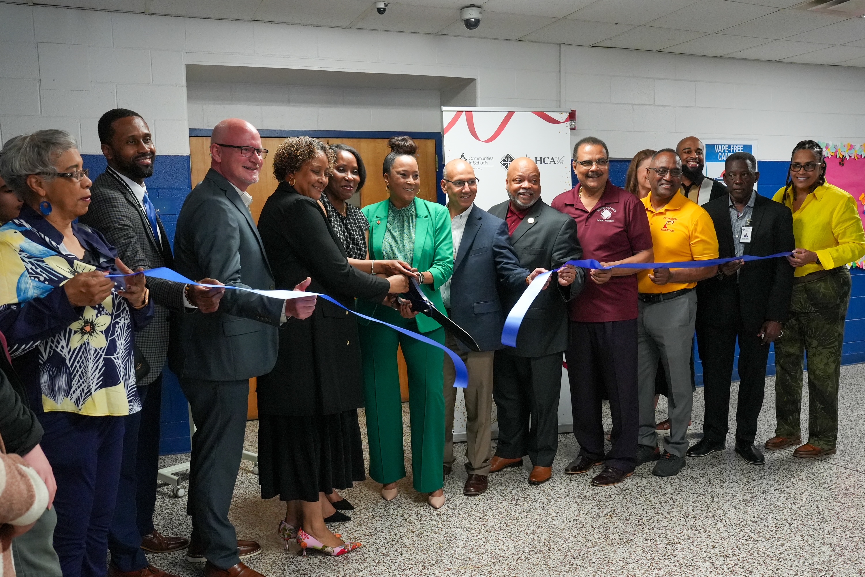 A group of adults cutting a ribbon in a school hallway