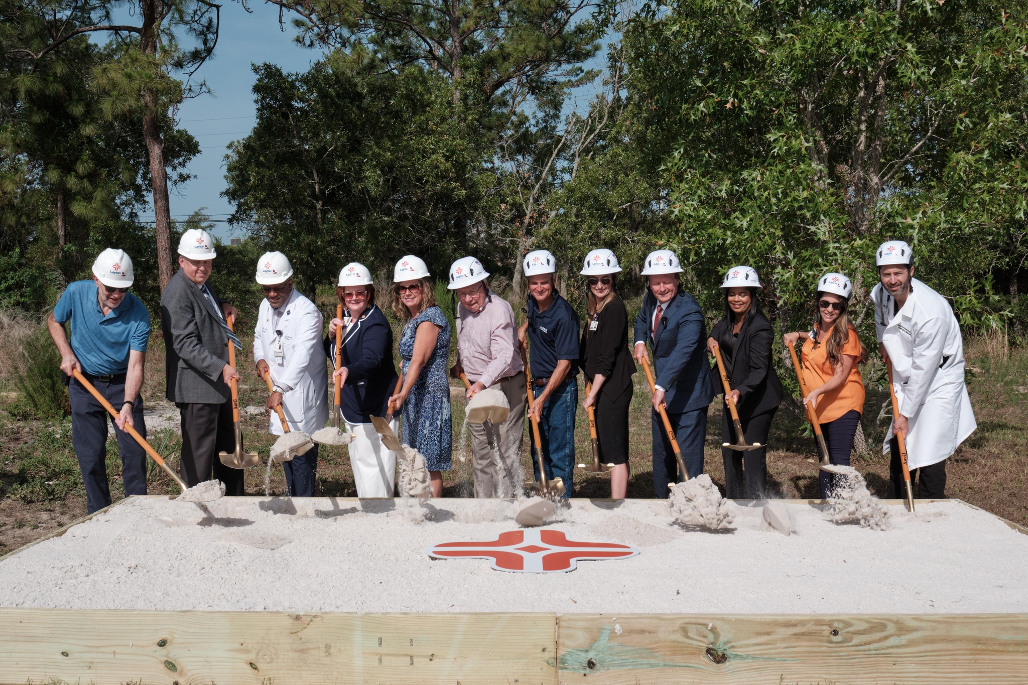 Group of individuals with construction hats holding shovels of sand surrounding the HCA logo.
