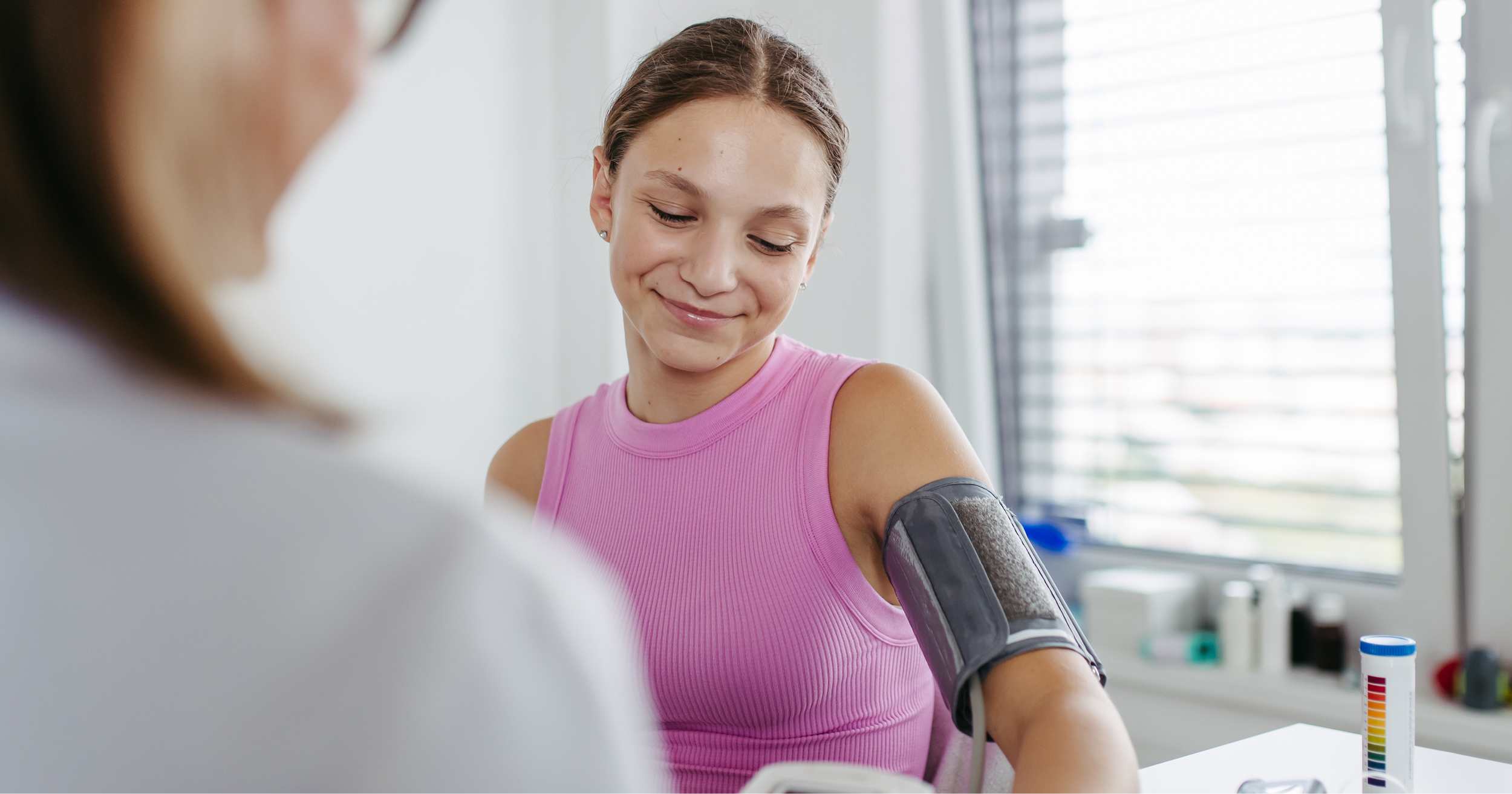 A person in a pink shirt getting a blood pressure test by a physician