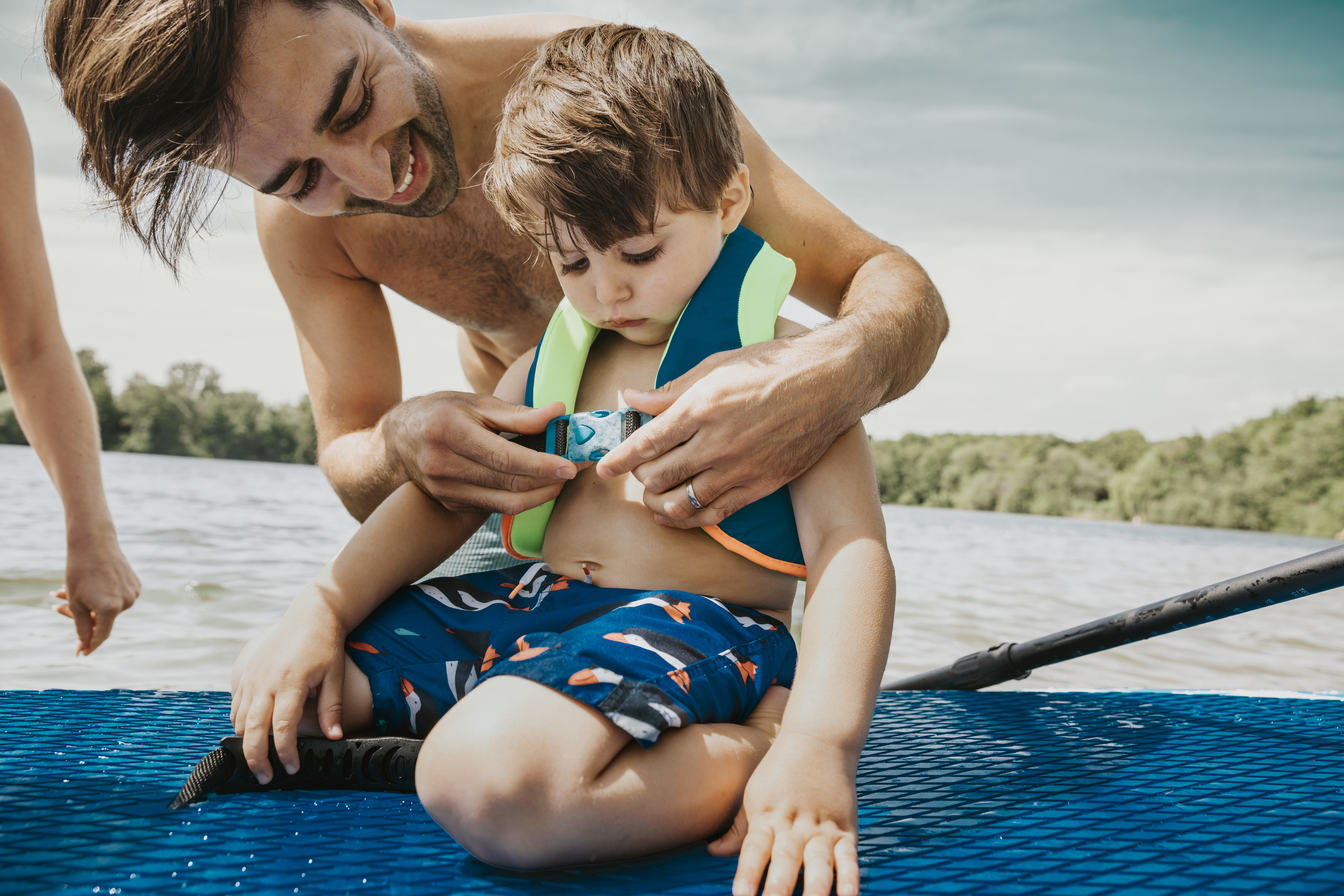 Father fastening life jacket for son in lake.