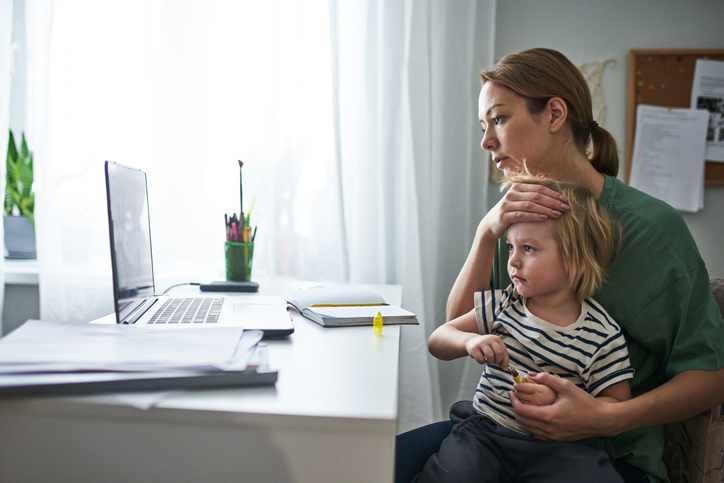 A young mother with a sick child consults a laptop during a telehealth appointment.
