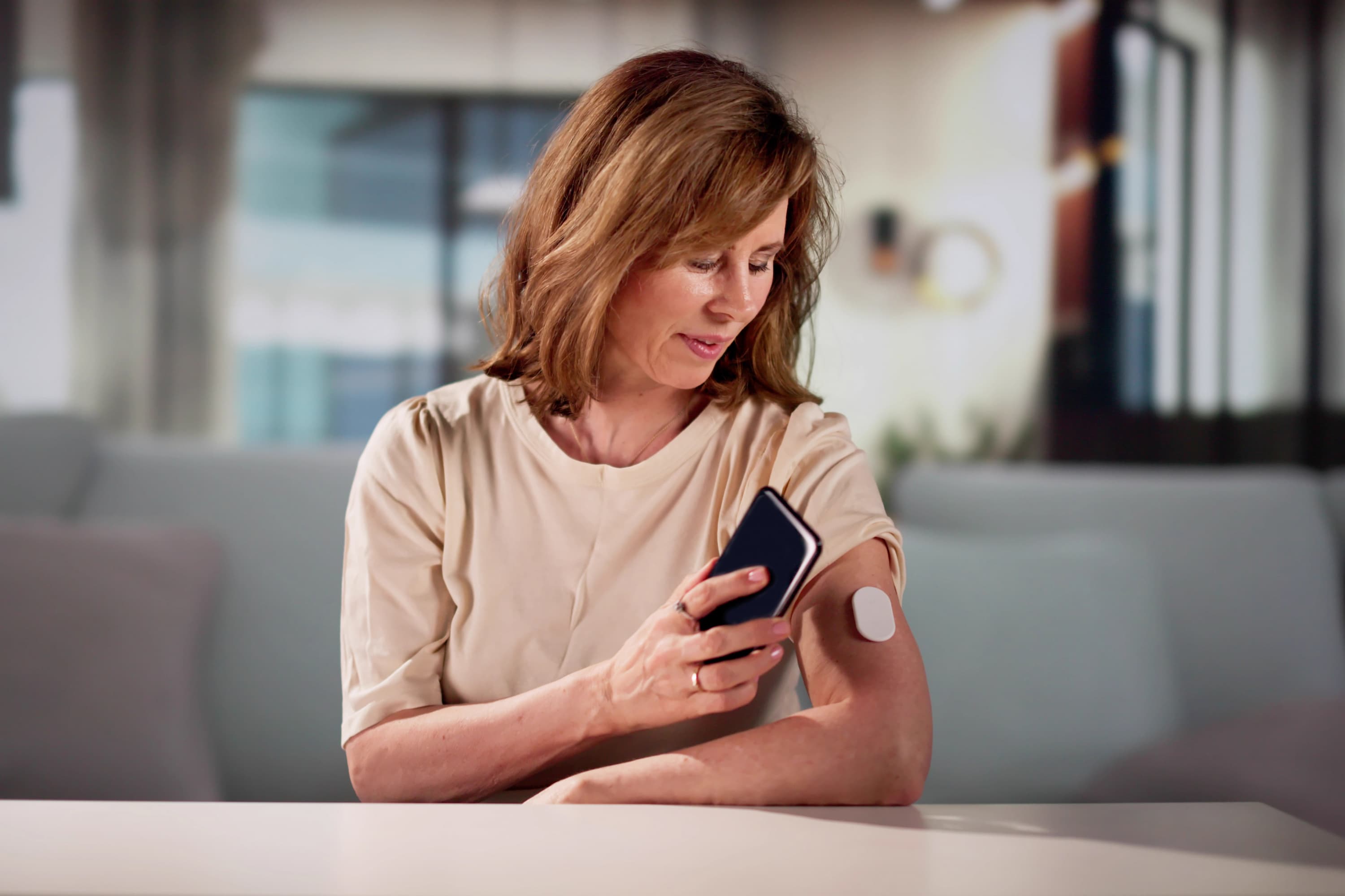 A woman holding her phone near a diabetes monitor on her arm to test her glucose and blood sugar.