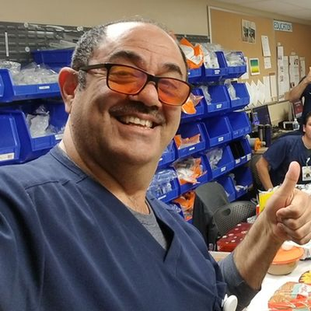 Ali is all smiles and expressing a thumbs-up, while wearing scrubs in the hospital.