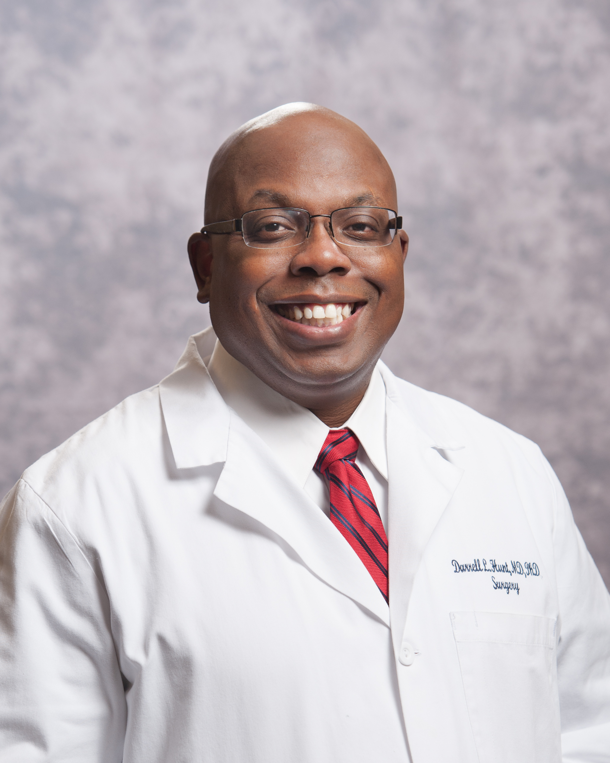 Dr. Darrell Hunt smiles while wearing a white lab coat and a red and blue stripe tie.