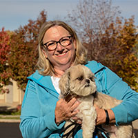 Lorna smiles while standing outside, holding her dog.