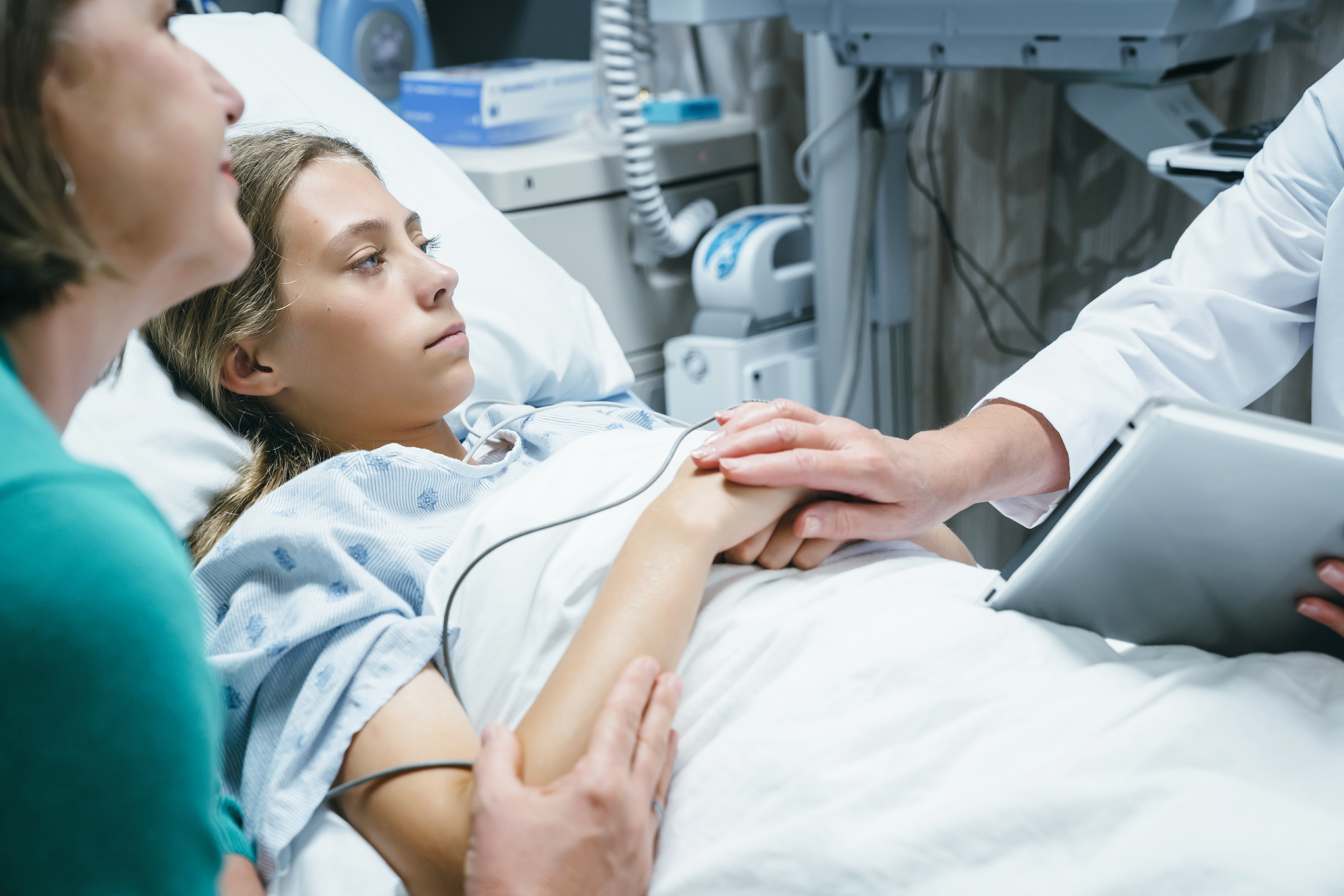 doctor with digital tablet comforting girl in hospital bed