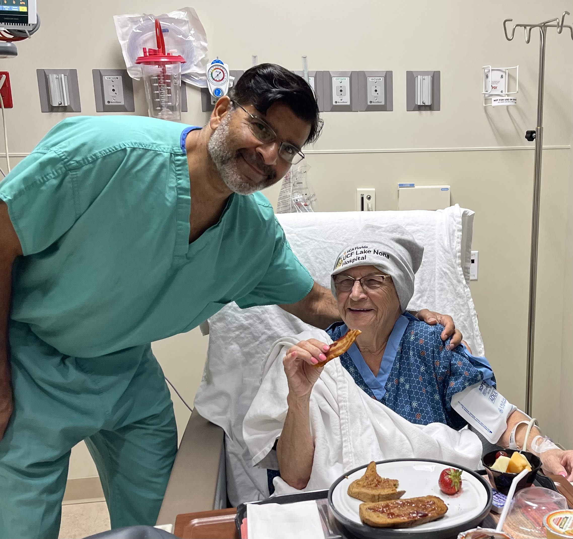 Christine before; Christine sitting in a hospital bed with dinner in a tray on her lap, her physician's arm around her shoulders