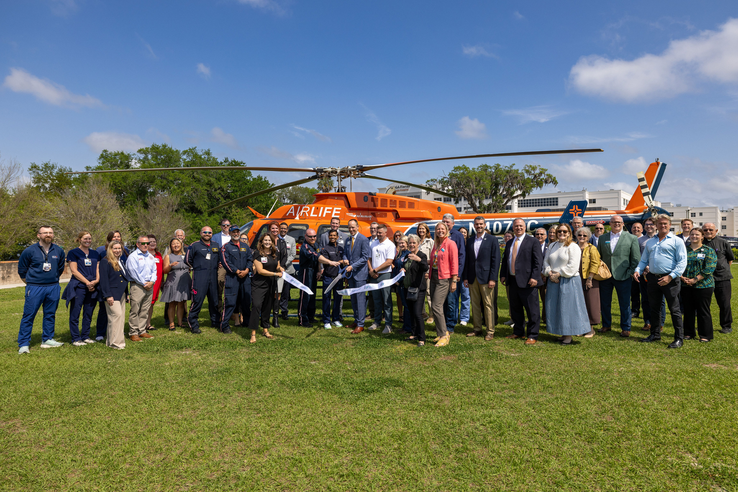 A flight crew member kneels in front of a group of smiling schoolchildren posing beside an orange AirLife medical helicopter.