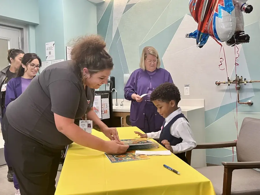 Female hospital staff surround young boy Payton seated at a table with books.