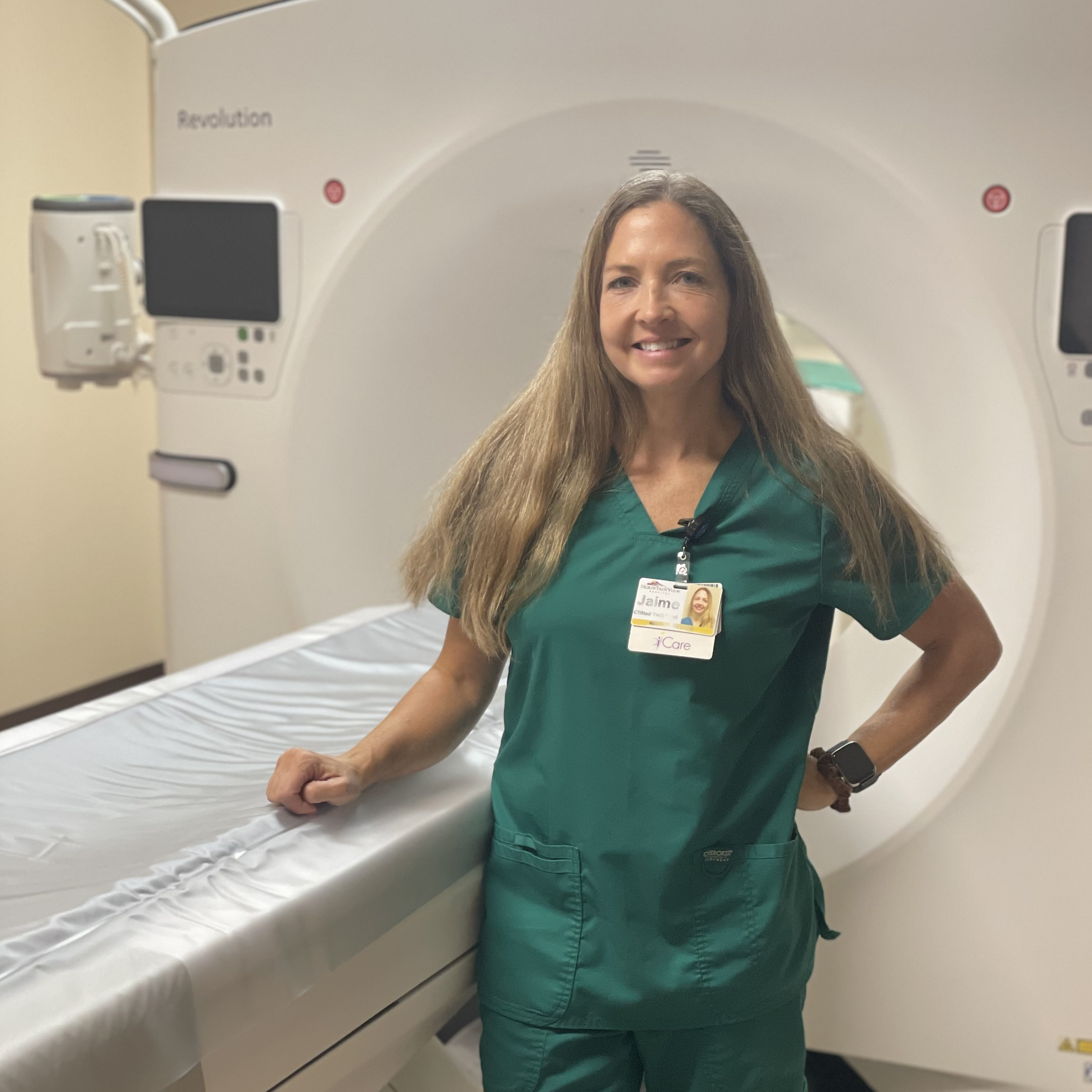 A female in green scrubs standing in front of a CT machine.