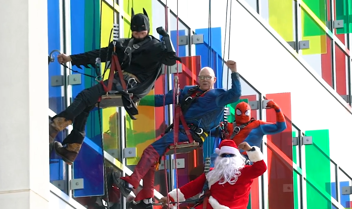 Window washer, suspended outside the building, dressed as Batman, Spider Man, Superman, and Santa Claus.