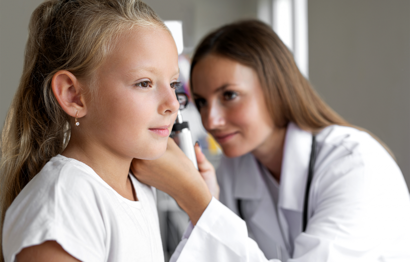 A female doctor checks the ears of a young girl, while performing a physical exam.