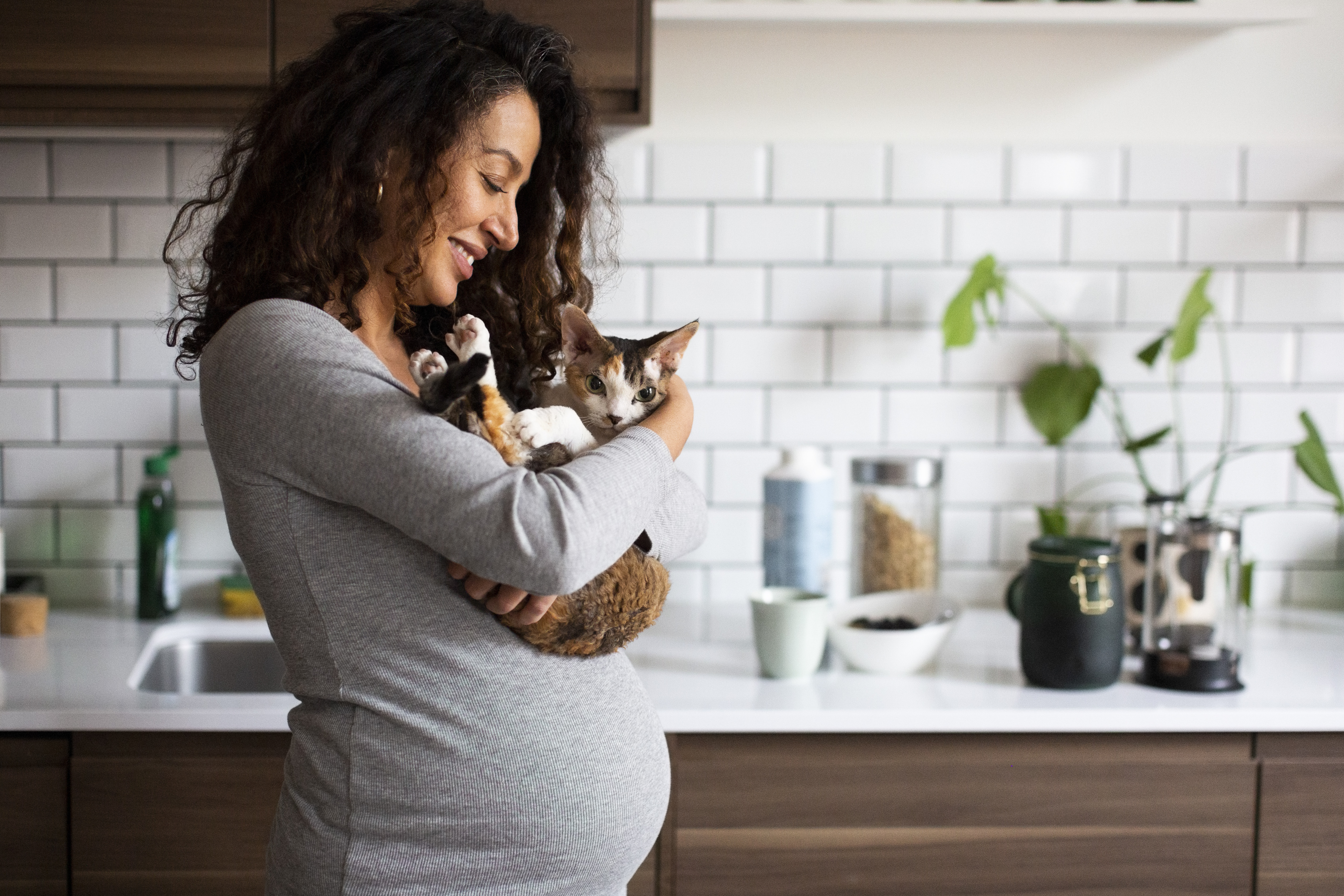 Expectant mom holds a cat and smiles in her kitchen.