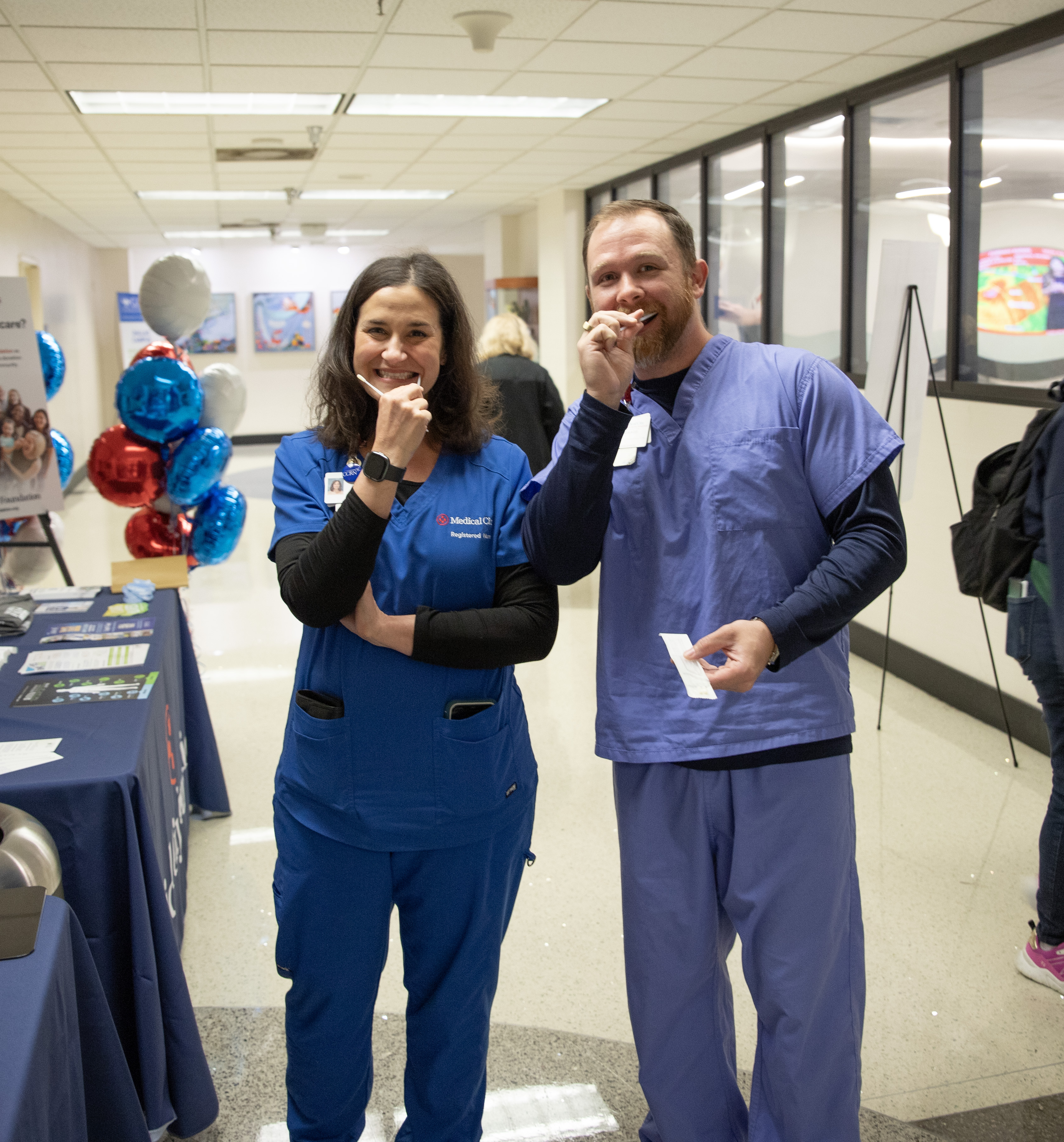 Medical City providers in hospital scrubs enjoying suckers at registry table.