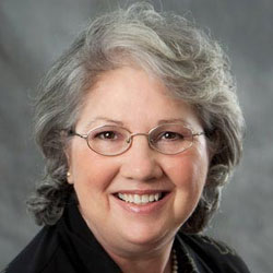 Peggy smiles while wearing glasses and a black blazer.