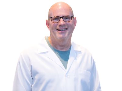 Dr. Timothy Duniho smiles for the camera, wearing a lab coat against a white backdrop.