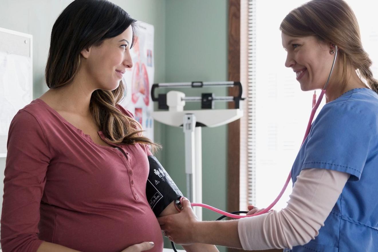 A smiling pregnant woman is examined by a female in hospital scrubs 