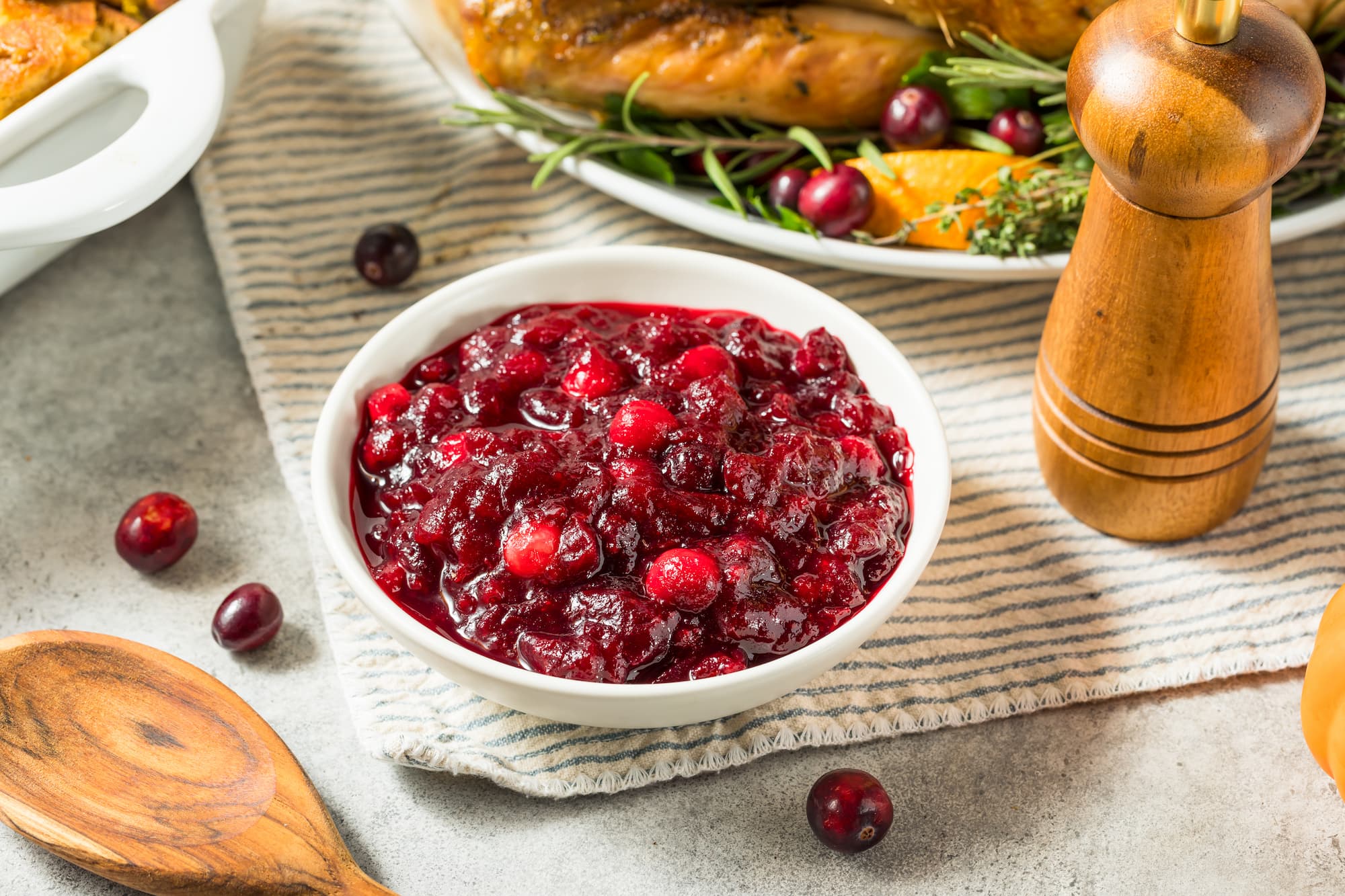 A bowl of homemade cranberry sauce on a placemat next to a plate of Thanksgiving food.