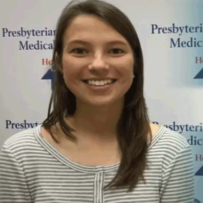 Anna Sniezek smiles while wearing a black and white stripe shirt, in front of a banner with the Presbyterian St. Luke's Medical Center logo.