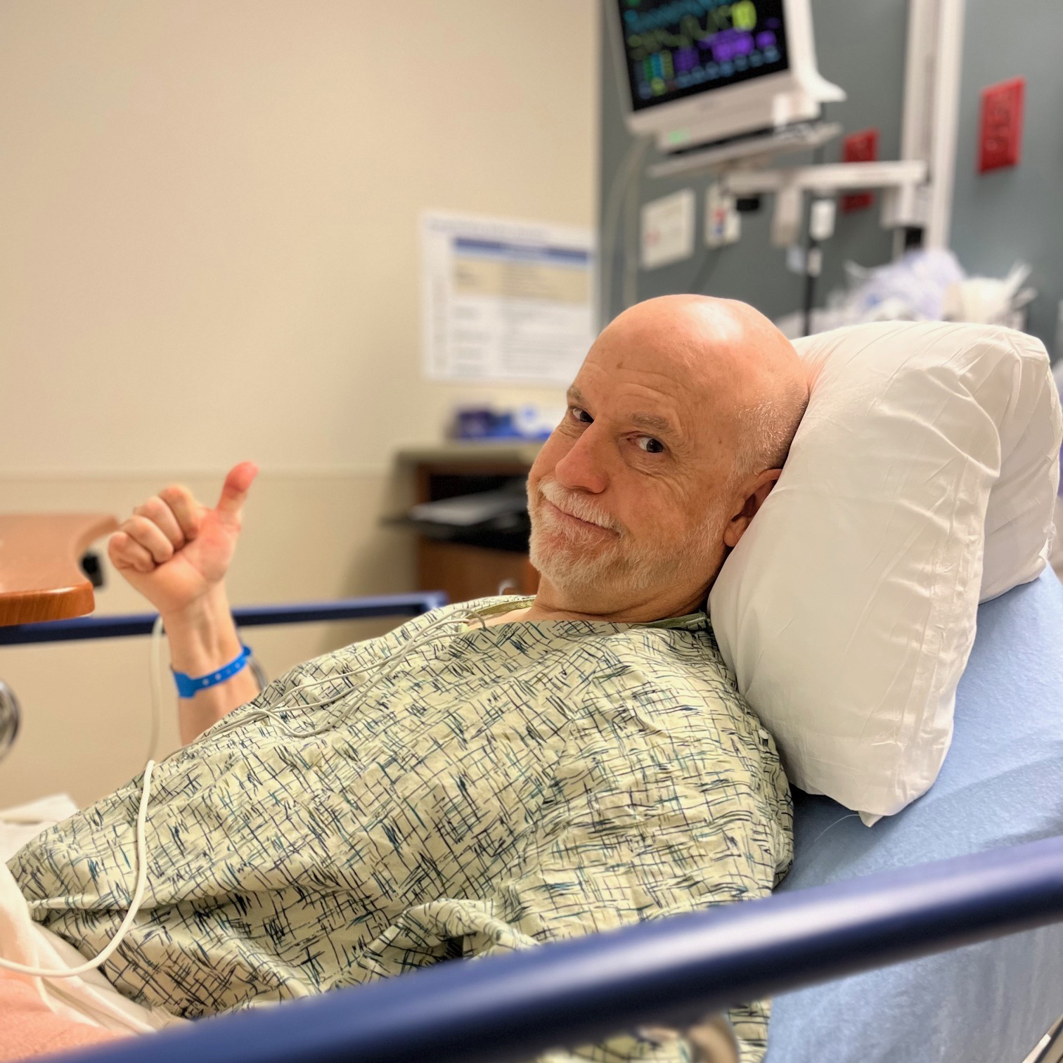 A patient in a hospital bed doing a thumbs up sign
