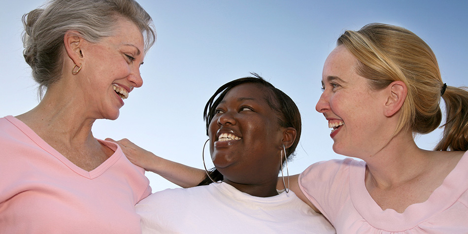A group of three women standing outdoors and smiling at each other.