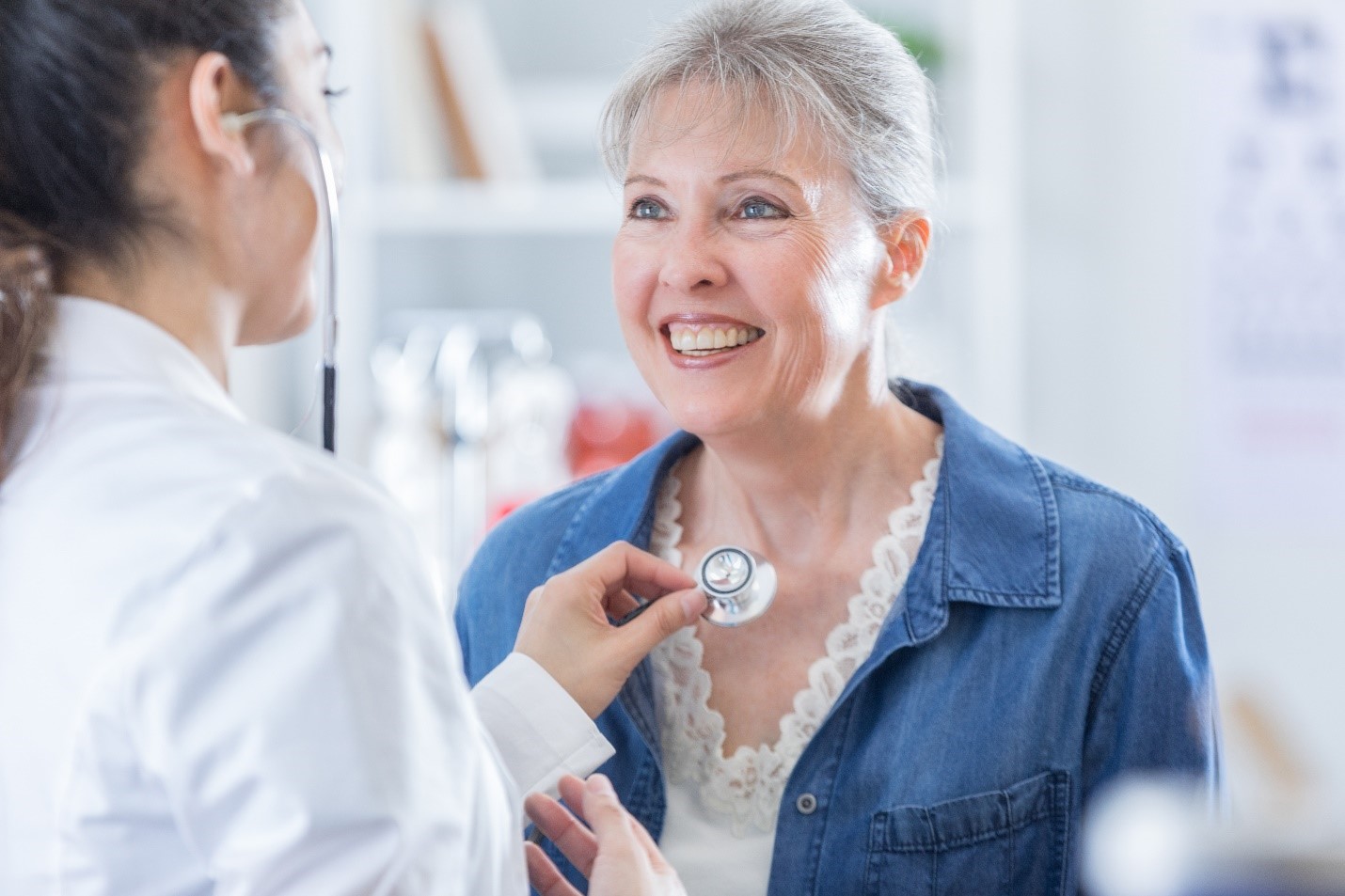 A physician listens to a smiling, senior woman's heartbeat with a stethoscope.