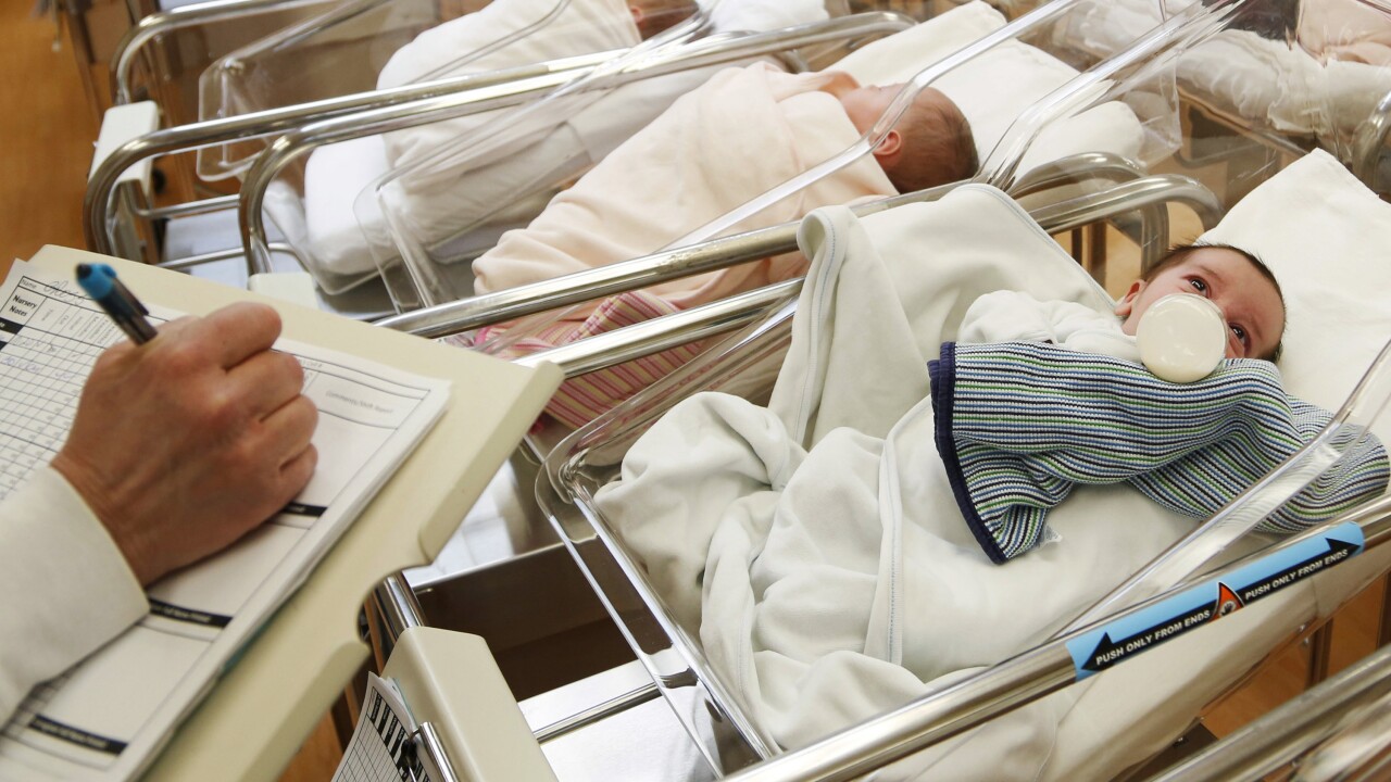 Doctor checks on healthy newborn in hospital crib.
