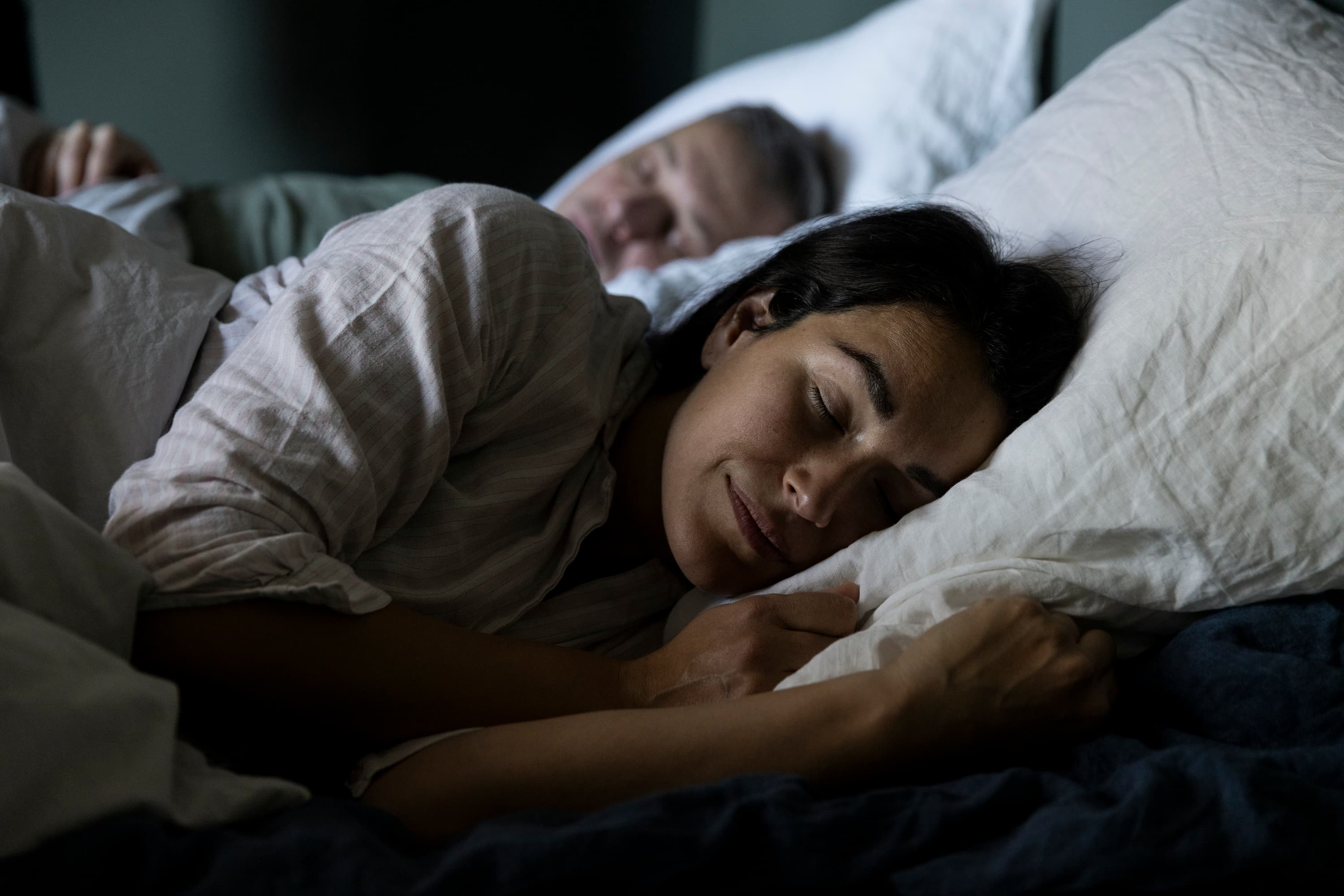 A woman and man sleep next to each other in a bed.