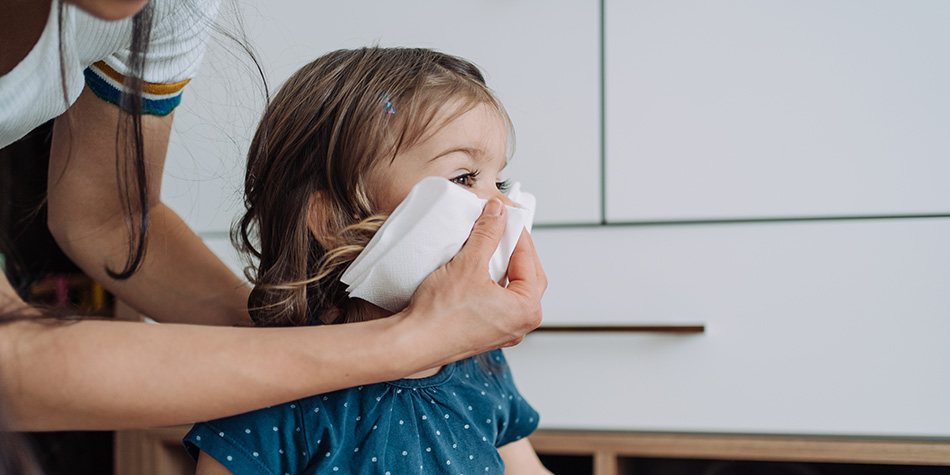 A mother wipes her child's nose with a tissue.
