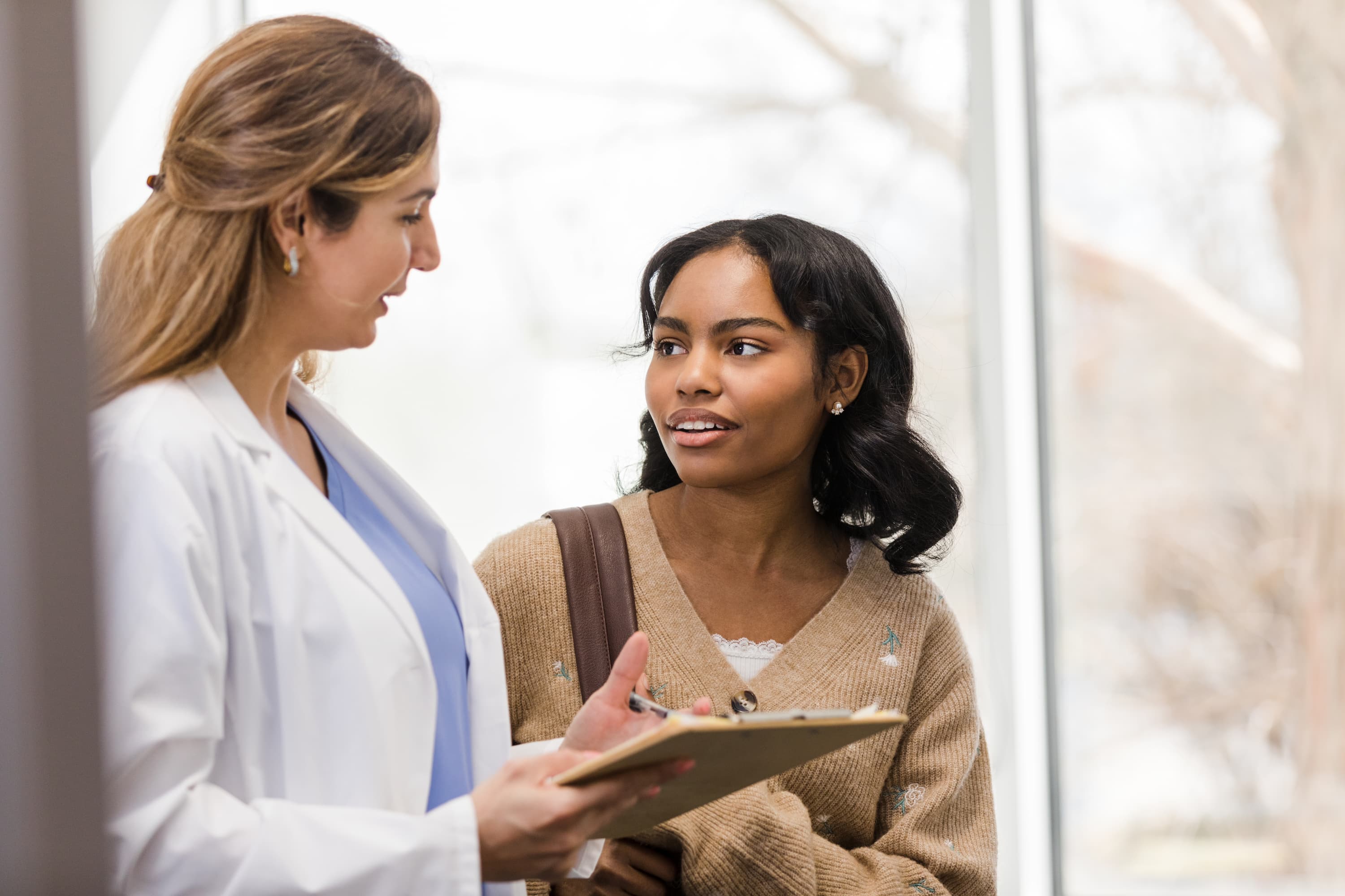 Woman speaking with a healthcare provider holding a clipboard during a medical visit.