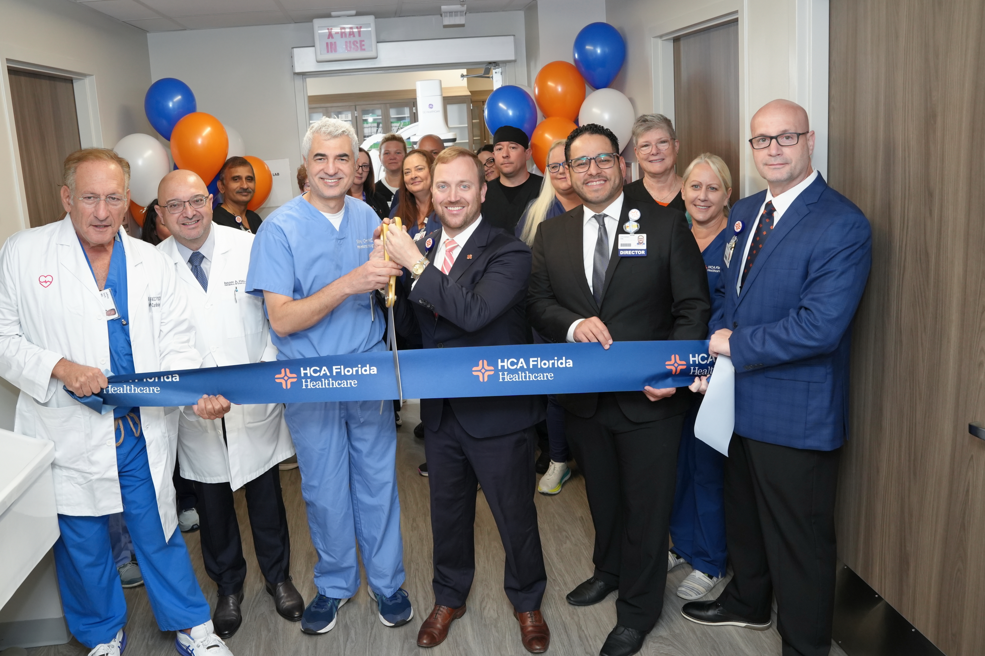 Sarasot Doctors Hospital team members stand in new cath lab hallway cutting a ceremonial blue ribbon with oversized scissors.