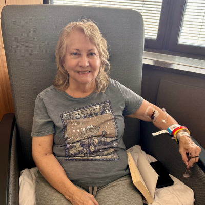 Kristie smiling, sitting in a chair with a book recovering from her brain surgery.