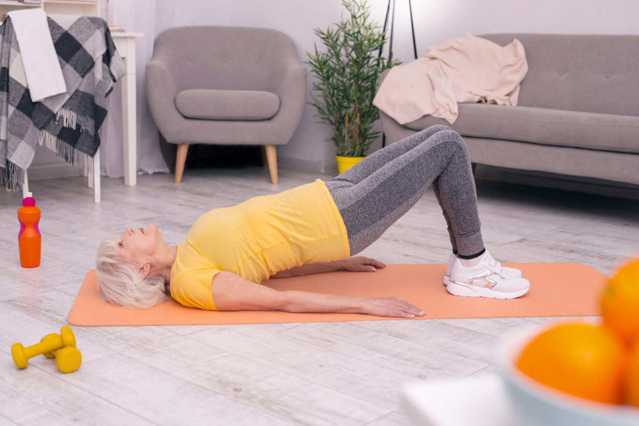 A senior woman doing floor exercises at home.