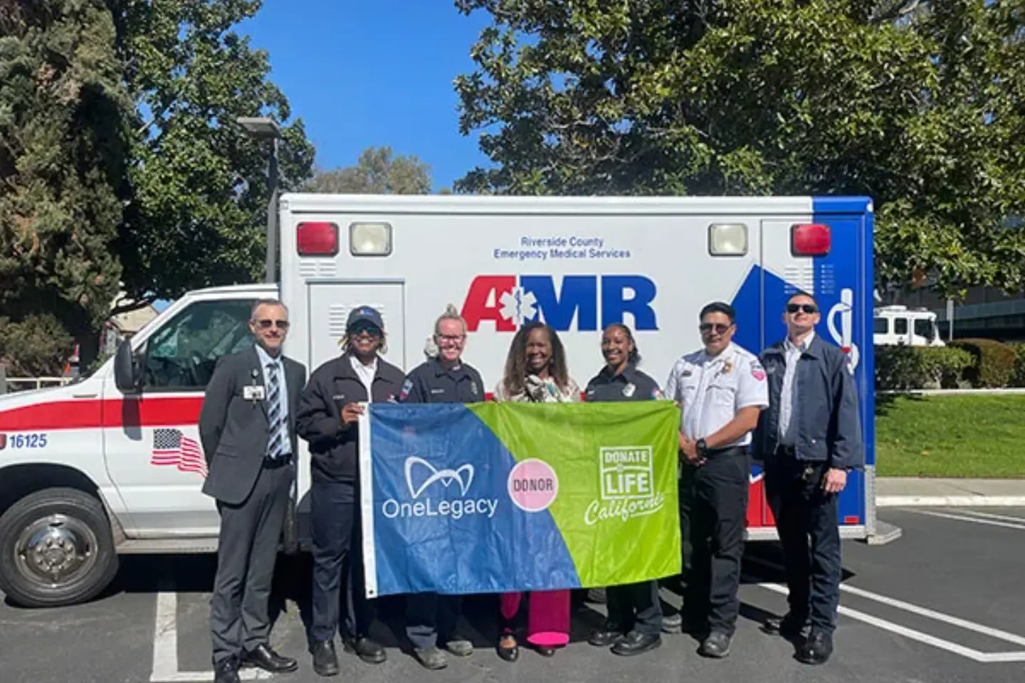 Medical professionals and Donate Life members smile while standing in front of an ambulance, holding the Donate Life flag.