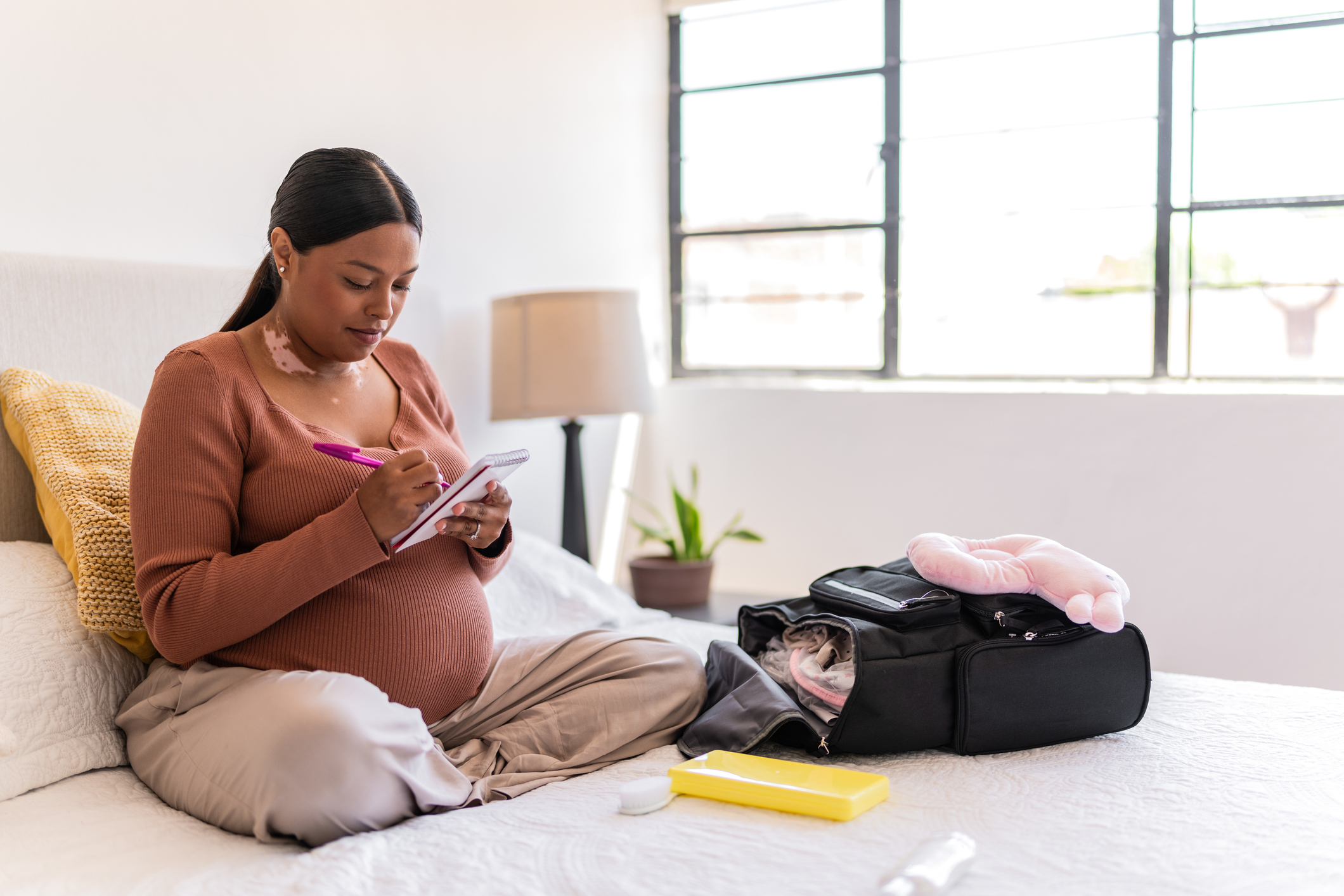 Pregnant woman packing baby clothes and maternity items into a backpack.