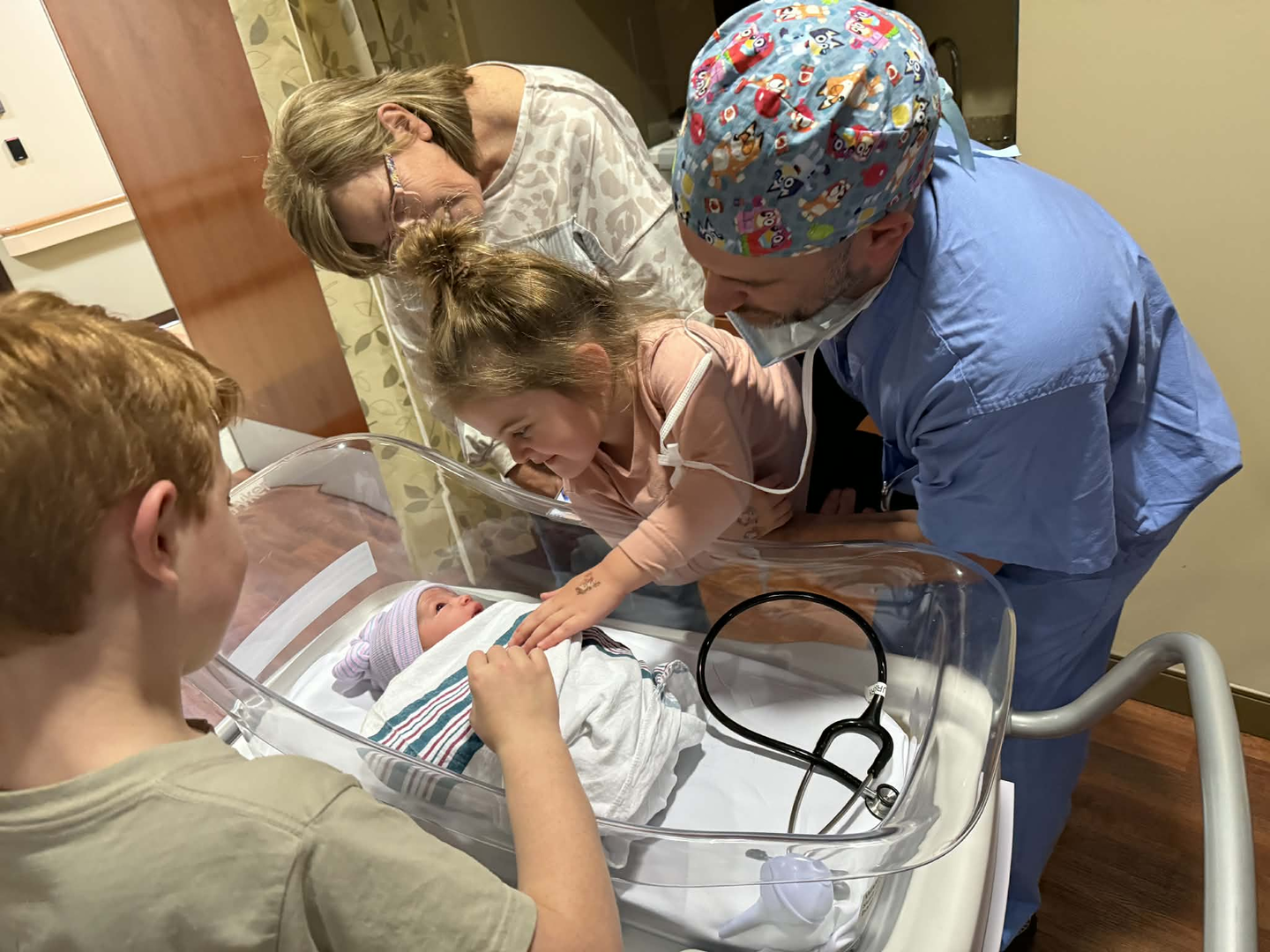 Photo showing of a baby in her hospital basinet surrounded with her family members visiting her for the first time.